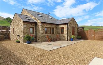 The sun shines on the cottage, surrounded by green hills.