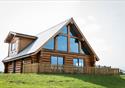 An outside view of a wooden cabin, sitting in the countryside.