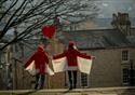 two people dressed in red with red hats walk the Georgian streets of Lancaster holding a red heart.