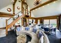 The high ceiling of a lodge with wooden beams.  A large curved comfortable sofa awaits guests.