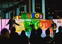 A bright stage at night with three performers on stage and an audience facing them.