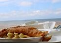 A plate of fish and chips against the backdrop of Blackpool beach on a sunny day.