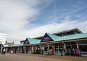 The single story Festival Market with corrugated turquoise roof sits under a cloudy blue sky