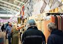 Customers walk through the market. One woman stops to speak to a trader about the carpets he is selling
