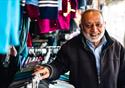 A male stallholder rest his hands on a rail of clothing he has for sale as he looks at the camera smiling