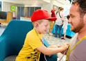 A boy uses a stethoscope to check the heart of his father.