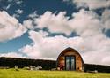 A pod sits in the sun, surrounded by green grass and fluffy clouds.