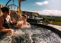 A couple enjoy the hot tub, with a glass of fizz, on sunny day.
