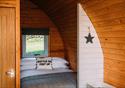 Inside the wooden pod, a comfortable looking double bed is decorated with a cushion reading 'kettle on, feet up.'