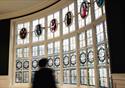 A curved stained glass window features a number of panels with impressions of and names of famous people in the arts