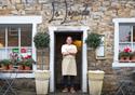 The chef stands proudly in the doorway of the restaurant, arms crossed.