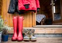 Sets of wellington boots and coats sit outside a wooden glamping pod, waiting for adventure.