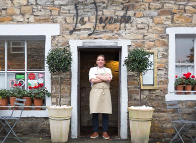 The chef stands proudly in the doorway of the restaurant, arms crossed.