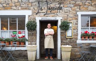 The chef stands proudly in the doorway of the restaurant, arms crossed.