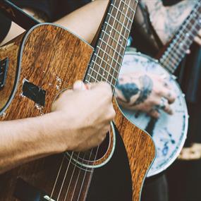 Person playing a banjo and another playing a dark wood acoustic guitar and another with a double bass