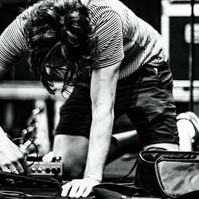 Black and white image of a person plugging in a pedalboard on stage