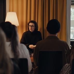 Long haired individual talking to a crowd