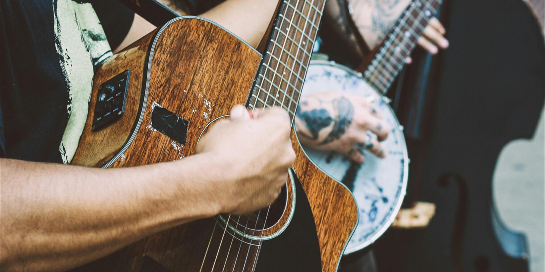 Person playing a banjo and another playing a dark wood acoustic guitar and another with a double bass