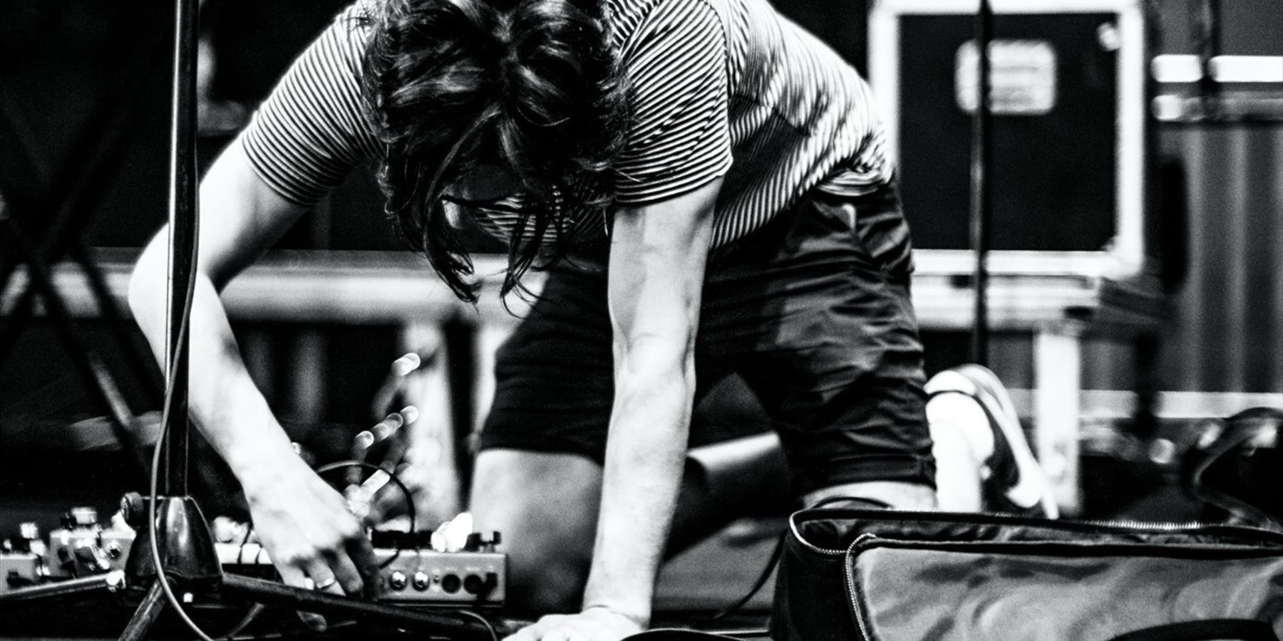 Black and white image of a person plugging in a pedalboard on stage