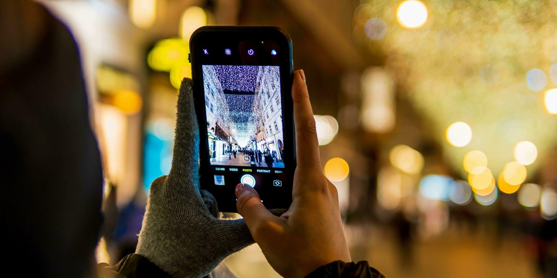 Person with one glove off taking a photo of a Christmas street light display