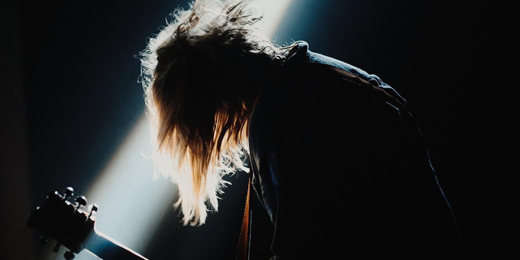 Person playing a guitar with a spotlight on them
