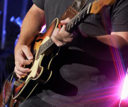 Man in black shirt playing a brown electric guitar