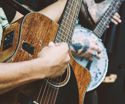 Person playing a banjo and another playing a dark wood acoustic guitar and another with a double bass