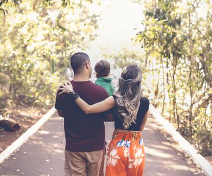 Young family walking in a light forest and carrying their toddler