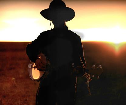 Silhouette of a person wearing a cowboy hat and playing a banjo