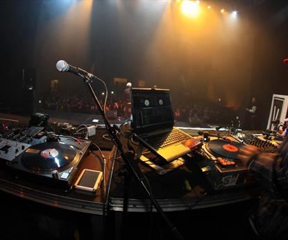 Person in a red hood DJing to a large crowd