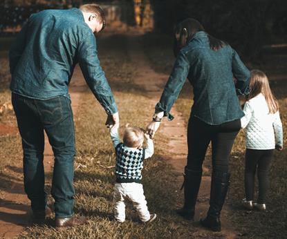 Young family walking a green forest and holding hands with their toddler