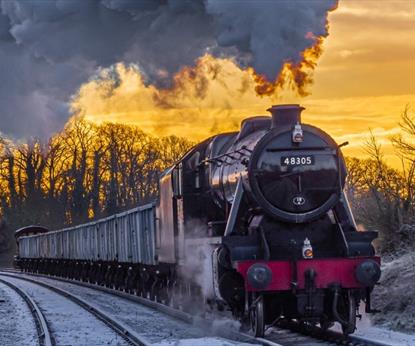 A steam train in the snow with sunset behind