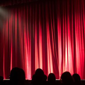 People sitting in a theatre in front of a red curtain