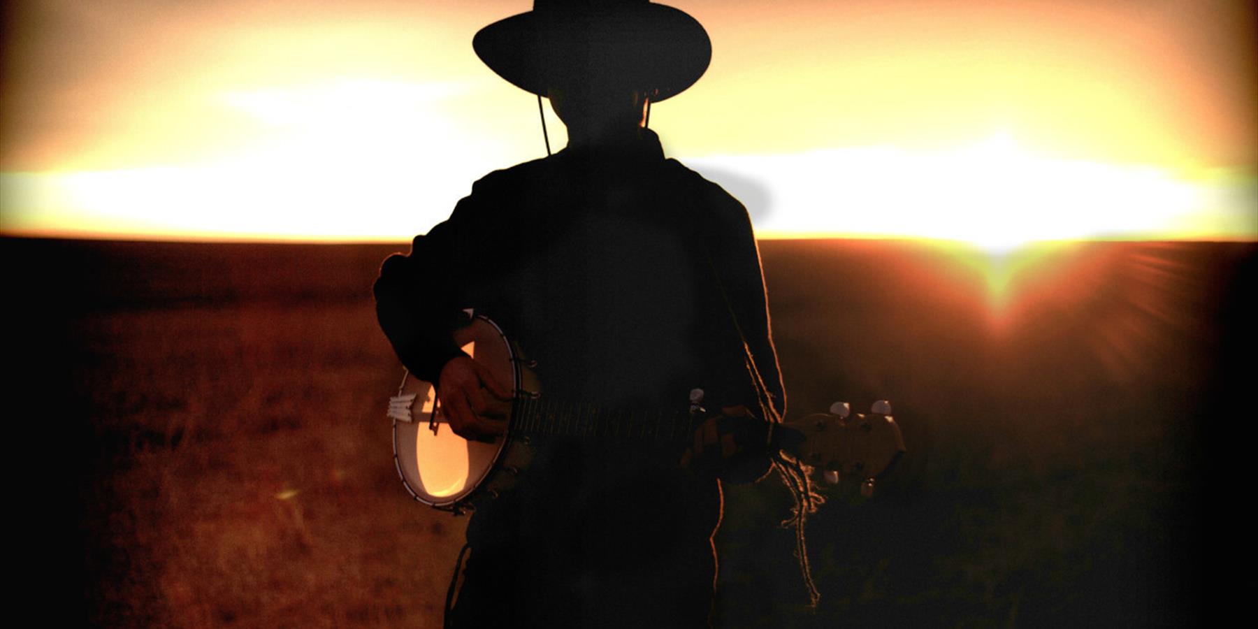Silhouette of a person wearing a cowboy hat and playing a banjo