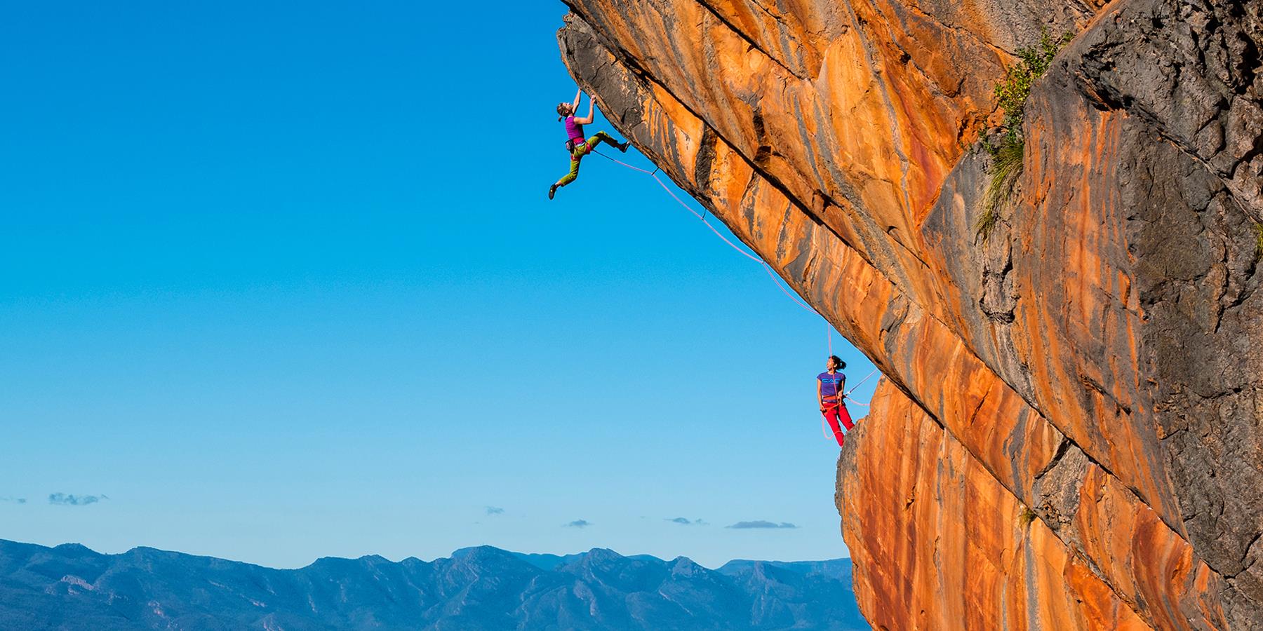 Two people climbing a high ledge
