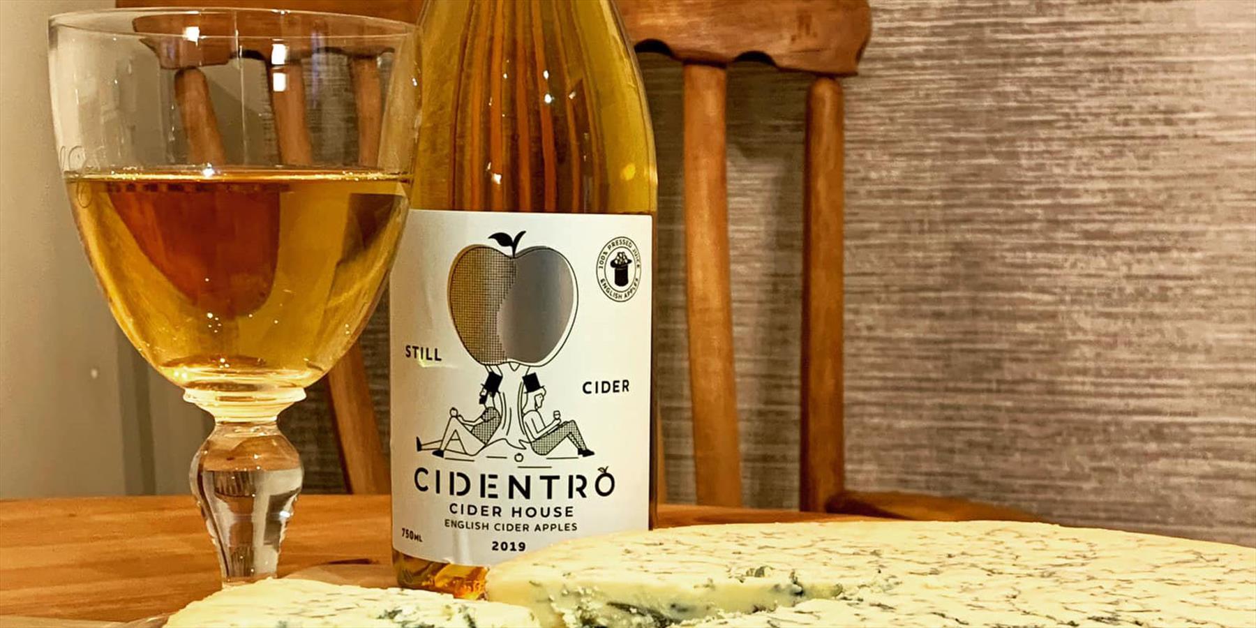A glass and bottle of cider with some stilton cheese on a table