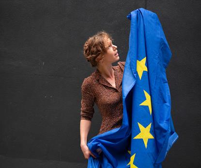 Performer Anna Clover is a white female, holding up an EU flag.