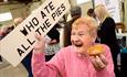 An older lady holding a 'who ate all the pies' sign