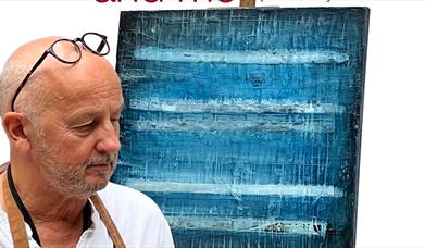 Artist and writer John Worth with artwork on an easel.