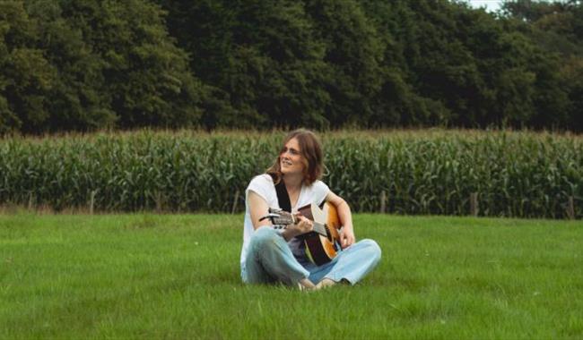Singer Anouska Assisi sitting in a field with her guitar