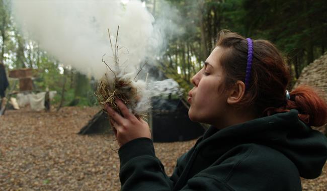 Person blowing on dried grass to create fire