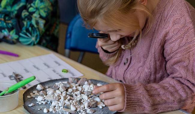 Girl examining stones with magnifying glass for archaeological adventure