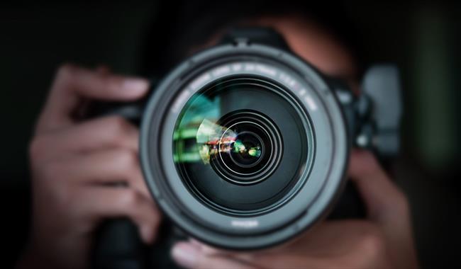 Looking down a camera lens, with person holding camera behind