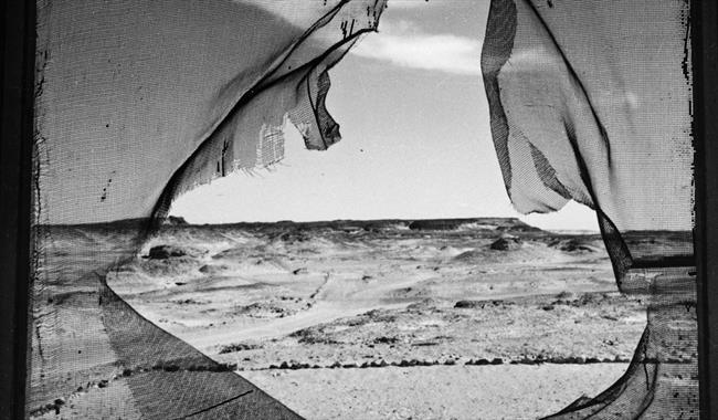 Black and white photograph featuring landscape seen through a whole in a canvas