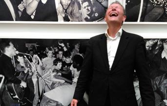 Gerry Colvin laughing in front of a photographic display