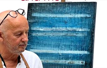 Artist and writer John Worth with artwork on an easel.