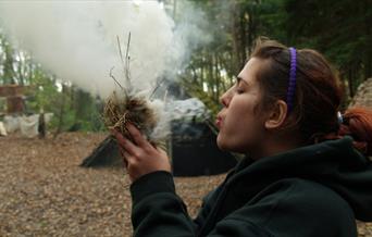 Person blowing on dried grass to create fire