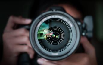 Looking down a camera lens, with person holding camera behind