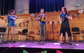 Folk musicians - Elye Cuthbertson, Danny Marshall and Mía Iles-Pérez on stage.
