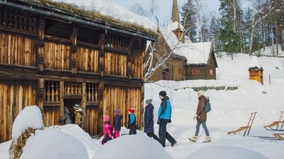 Adults and children entering a historic timber house by Garmo stave church.